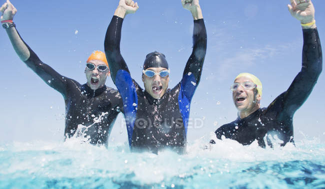 Confident and strong triathletes in wetsuits splashing in waves — Stock Photo