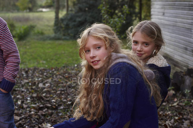 Chicas sonrientes sentadas en el patio trasero y mirando a la cámara - foto de stock