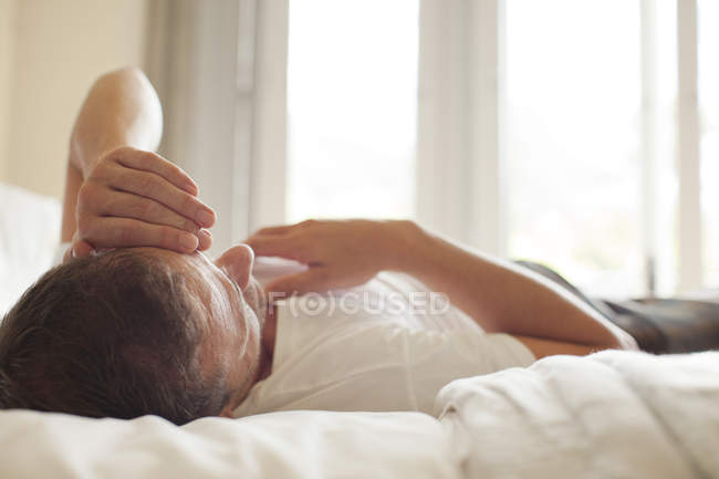 Homem deitado na cama com a cabeça nas mãos — Fotografia de Stock