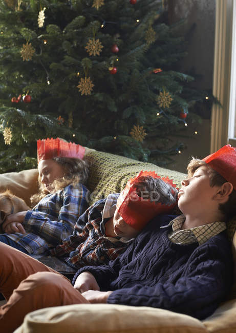 Niños en coronas de papel durmiendo en sofá - foto de stock