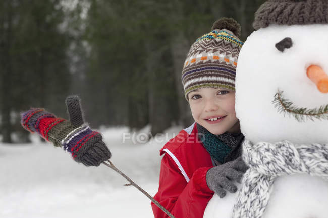 Fechar-se de menino sorridente atrás boneco de neve — Fotografia de Stock