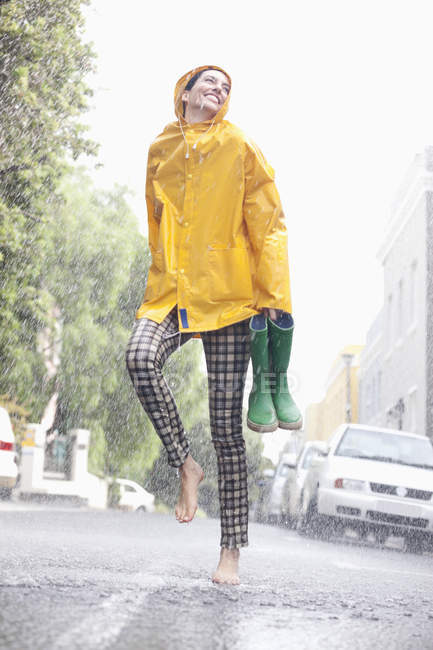 Счастливая женщина танцует босиком на дождливой улице — стоковое фото