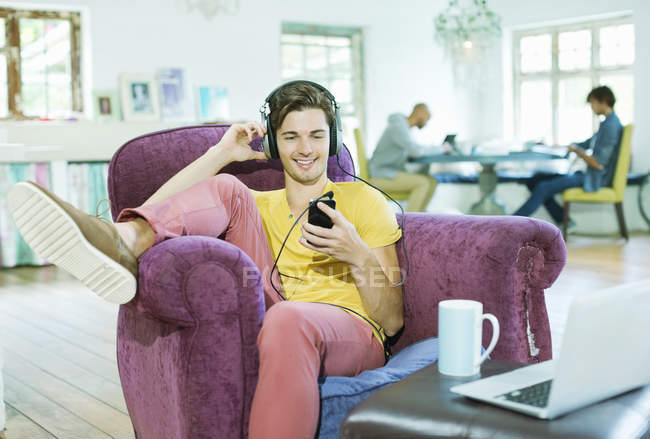 Young man listening to headphones in armchair — Stock Photo