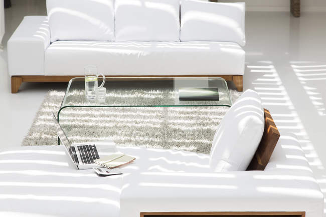 Ordenador portátil, sofás y mesa de centro en la sala de estar moderna - foto de stock