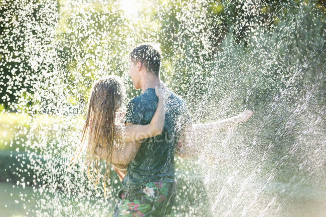 Rear view of couple playing in sprinkler in backyard — Stock Photo