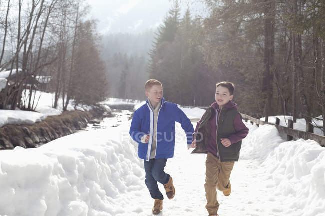 Мальчики держатся за руки и бегают по снежной полосе — стоковое фото