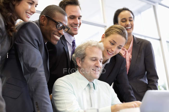 Улыбающиеся деловые люди делятся ноутбуком на встрече в современном офисе — стоковое фото