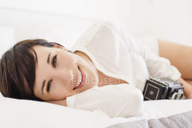 Retrato de mulher sorridente com câmera vintage na cama — Fotografia de Stock