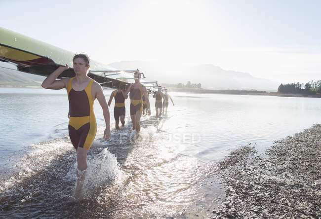 Rowing crew carrying scull out of lake — Stock Photo