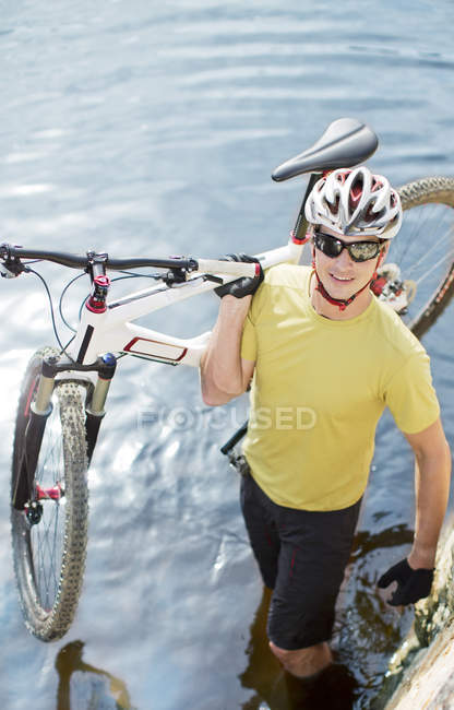 Man carrying mountain bike in river — Stock Photo