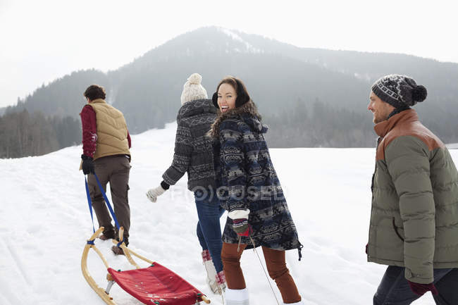 Felices amigos tirando de trineos en el campo nevado - foto de stock