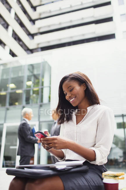 Geschäftsfrau sitzt mit Handy draußen auf Bank — Stockfoto