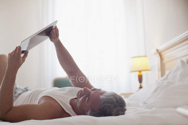 Hombre acostado en la cama y utilizando tableta digital - foto de stock