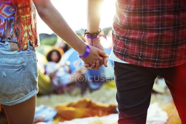 Primer plano de pareja cogida de la mano fuera de las tiendas de campaña en el festival de música - foto de stock