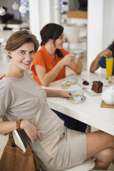 Mujer embarazada tomando una taza de café con amigos - foto de stock