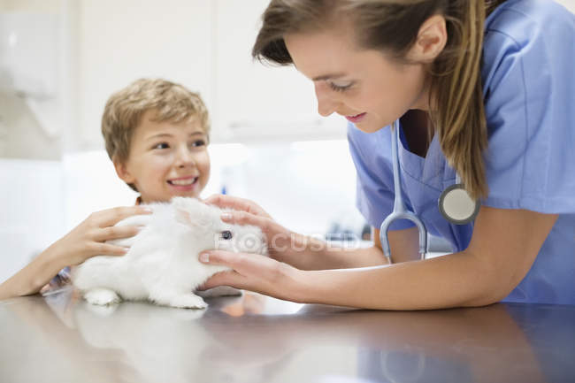 Veterinario caucásico examinando conejo con chico, primer plano - foto de stock
