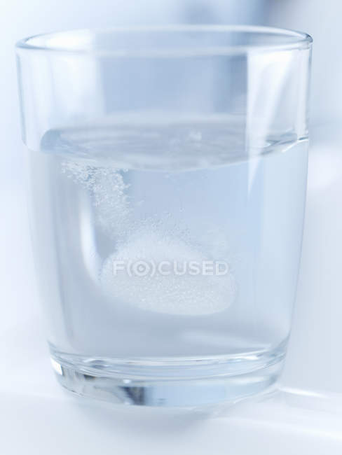 Gros plan de la pilule pétillante dans un verre d'eau — Photo de stock
