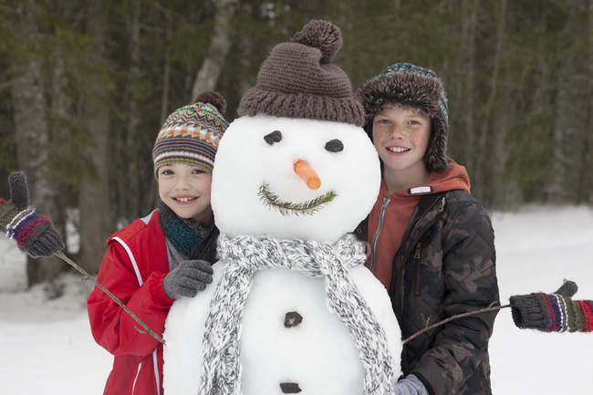Portrait of happy boys posing with snowman — Stock Photo