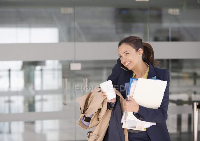 Улыбающаяся деловая женщина многозадачная по мобильному телефону с кофе и бумажной работой — стоковое фото