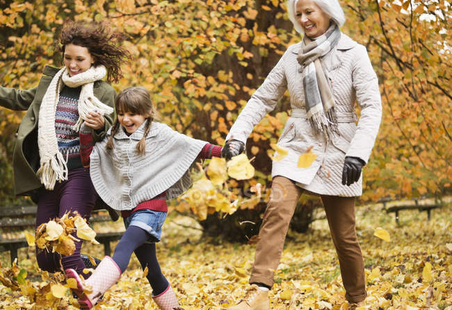 Tres generaciones de mujeres jugando en hojas de otoño - foto de stock