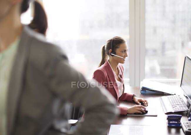 Mujer de negocios con auriculares en el escritorio en la oficina moderna - foto de stock
