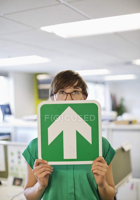 Businesswoman holding arrow sign in office — Stock Photo