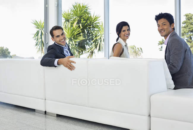 Ділові люди посміхаються на дивані в сучасному офісі — стокове фото
