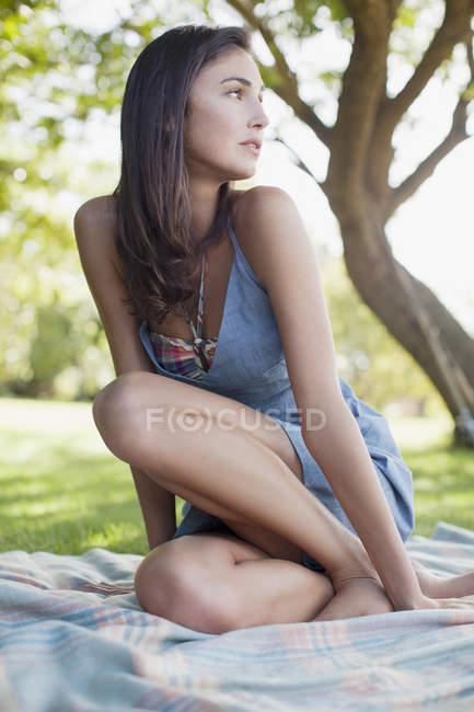 Pensive woman sitting on blanket in grass — Stock Photo