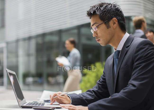 Geschäftsmann arbeitet am Laptop vor Bürogebäude — Stockfoto