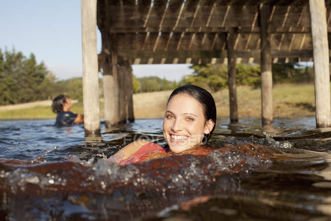 Retrato de una mujer sonriente nadando en el lago bajo el muelle - foto de stock