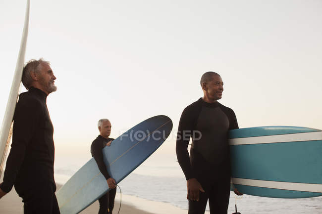 Older surfers carrying boards on beach — Stock Photo