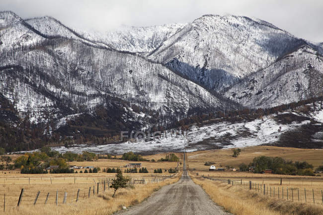 Сельская дорога, ведущая в заснеженные горы — стоковое фото