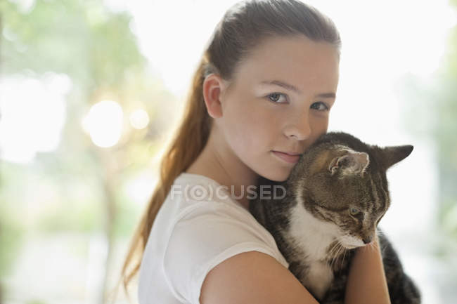 Chica sosteniendo gato contra fondo borroso - foto de stock