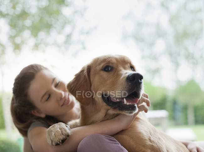 Улыбающаяся девушка обнимает собаку на улице — стоковое фото