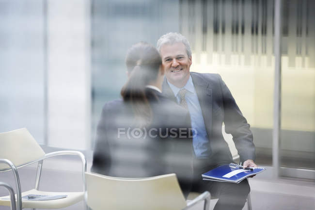 Усміхнений бізнесмен розмовляє з бізнес-леді в сучасному офісі — стокове фото