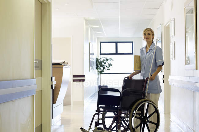 Медсестра штовхає інвалідне крісло в лікарняному коридорі — стокове фото