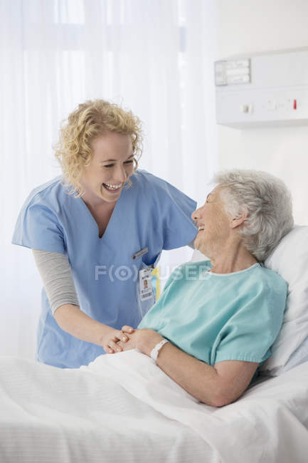 Enfermera y paciente mayor hablando en la habitación del hospital - foto de stock