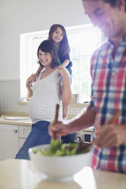 Pregnant mother and daughter watching father toss salad — Stock Photo