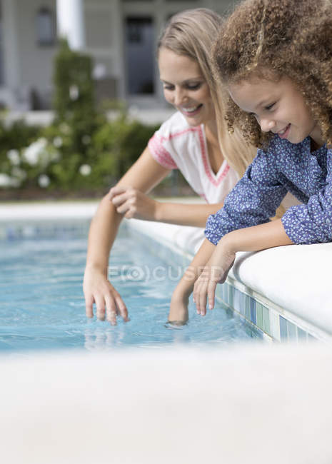 Mother and daughter dipping fingers in swimming pool — Stock Photo