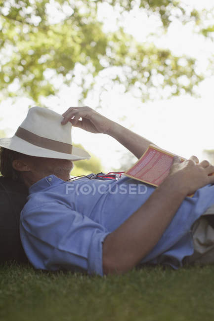 Человек дремлет в траве с книгой и лицом в шляпе — стоковое фото