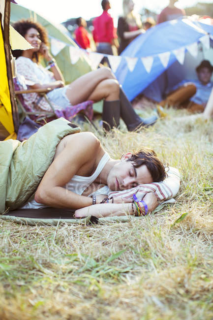 Hombre en saco de dormir durmiendo fuera de tiendas de campaña en el festival de música - foto de stock