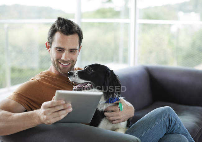 Homem de estimação cão e usando computador tablet em casa moderna — Fotografia de Stock
