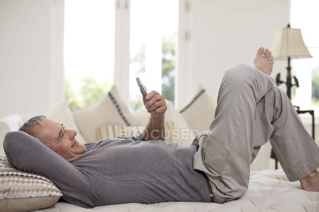Uomo anziano utilizzando il telefono cellulare sul letto — Foto stock