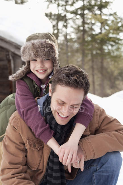 Retrato de un hijo feliz abrazando al padre en la nieve - foto de stock