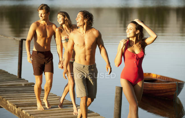 Coppie sorridenti che camminano sul molo sul lago — Foto stock