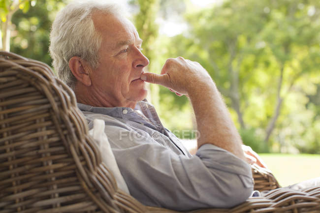 Pensativo hombre mayor sentado en sillón de mimbre en el porche - foto de stock