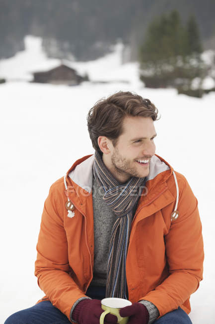 Hombre sonriente bebiendo café en el campo cubierto de nieve - foto de stock