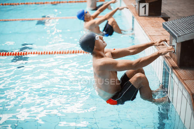Nadadores preparados en el bloque de salida en la piscina - foto de stock