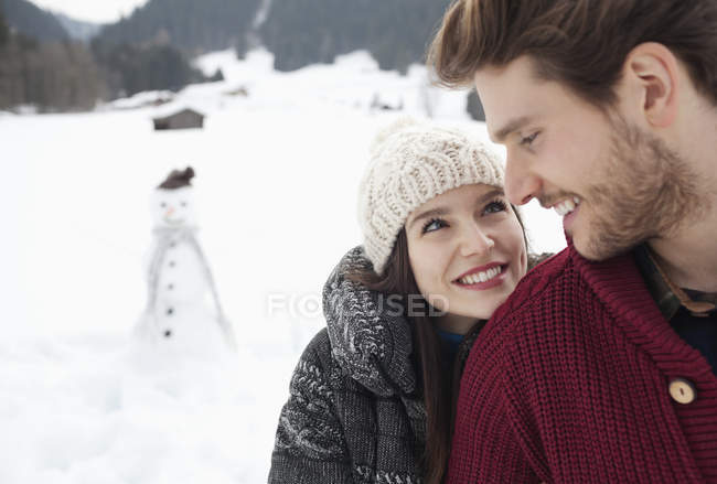Primer plano de feliz pareja en el campo nevado con muñeco de nieve - foto de stock