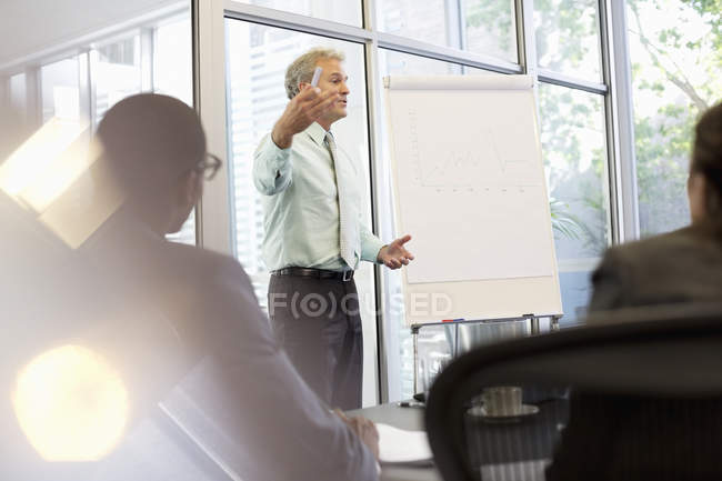 Hombre de negocios haciendo gestos en el rotafolio en la reunión en la oficina moderna - foto de stock